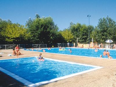 Piscina all'aperto con bagnanti sotto il sole estivo.