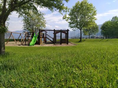 Parco giochi con scivolo verde, altalene e alberi in una giornata soleggiata.