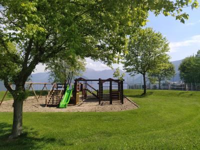 Parco giochi con scivolo verde e altalene, circondato da alberi e montagne.