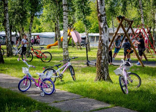 Bambini giocano in un parco con biciclette e altalene.