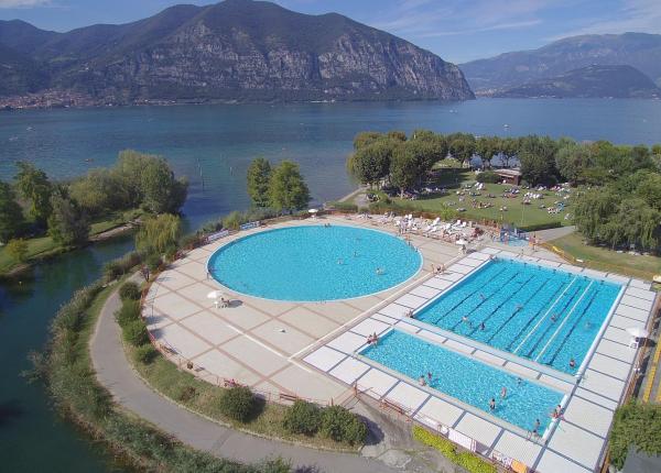 Piscina all'aperto vicino a un lago con montagne sullo sfondo.