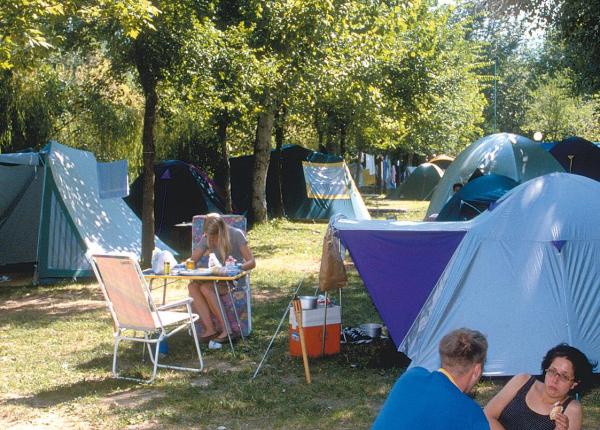 Persone che campeggiano in una foresta con tende e attrezzature da campeggio.