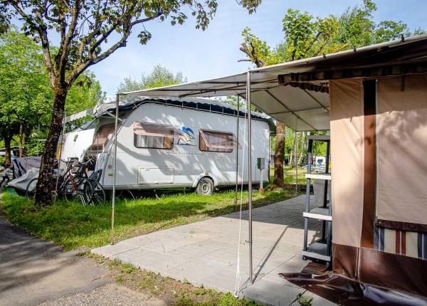 Campeggio con roulotte, biciclette e veranda in un ambiente verde.