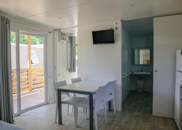 Interno moderno con tavolo, sedie, TV e accesso al balcone.