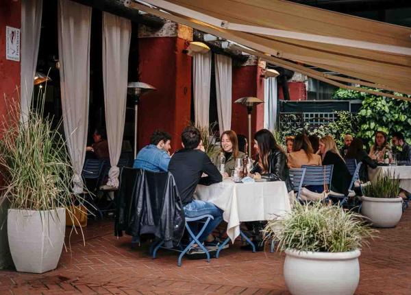 Persone che cenano all'aperto in un ristorante con tavoli e piante.
